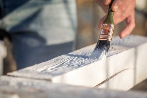 male hand paints with white paint on wood